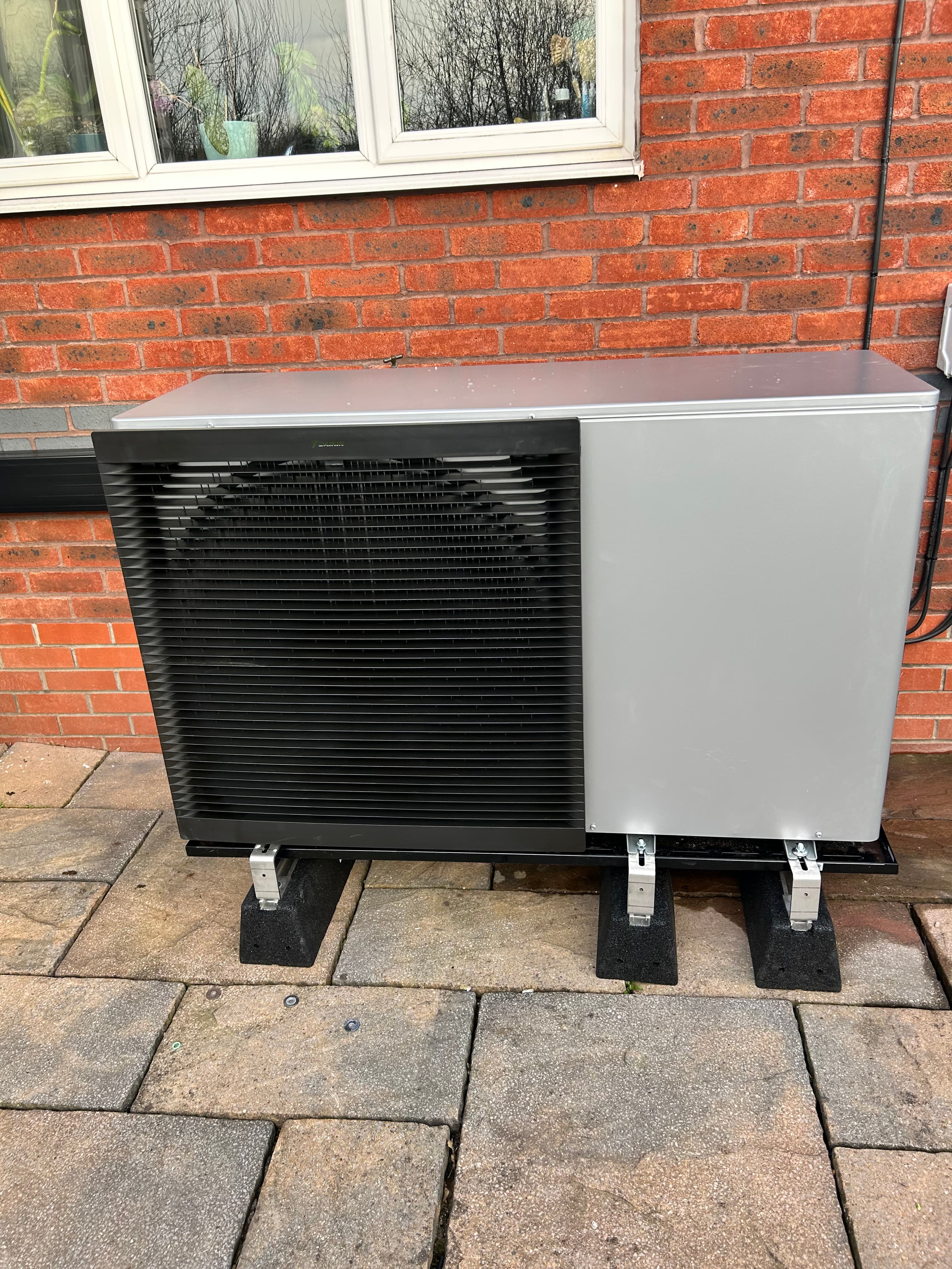 Modern air source heat pump installed on anti-vibration feet outside a home