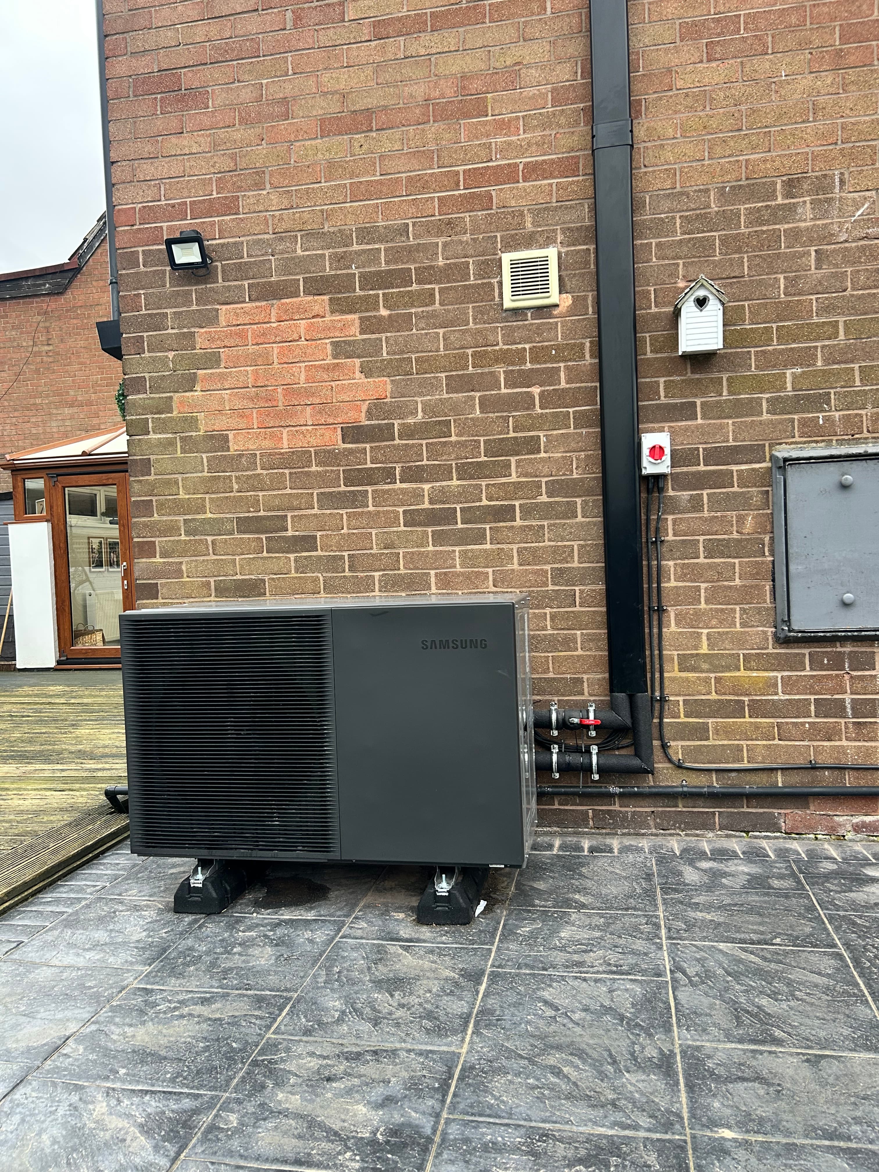 Samsung air source heat pump installed beside a brick home